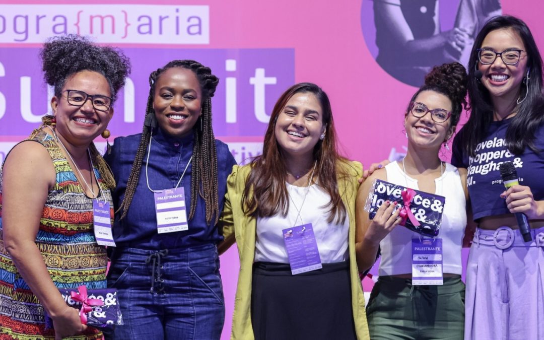 Imagem com as quatro participantes do Painel, junto com a Iana, com o fundo do palco do painel.