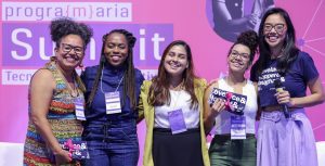 Imagem com as quatro participantes do Painel, junto com a Iana, com o fundo do palco do painel.
